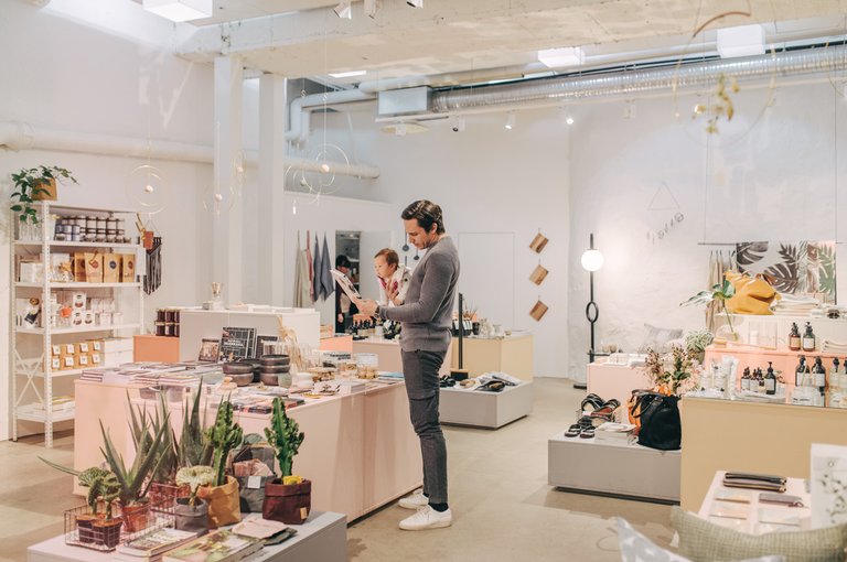 A man is shopping in Stockholm. He is holding his toddler in om arm and browsing through objects with the other.