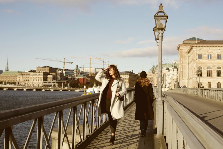 A woman is walking over the bridge to Skeppsholmen in Central Stockholm. She´s dressed in a white coat ans is looking to the horizon.