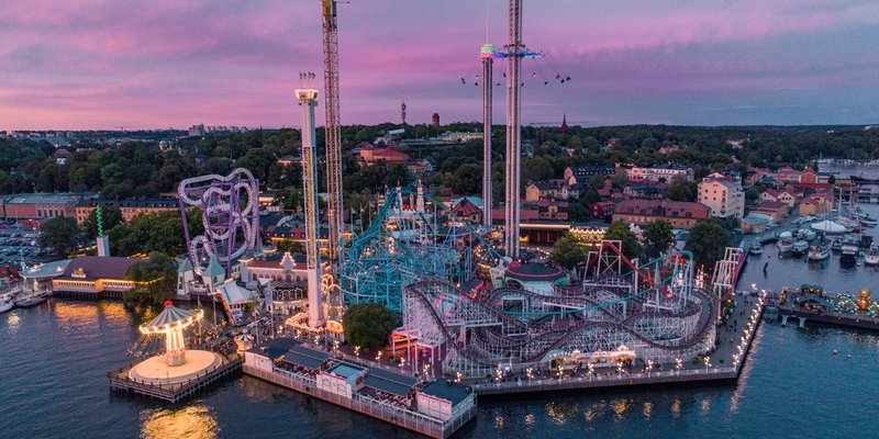 The amusement park Gröna Lund at night, all the attractions are lit up in pretty neon colours and the park is surrounded by water.