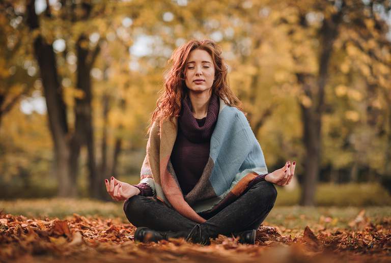 A woman sitting in a meditation pose in a forest.