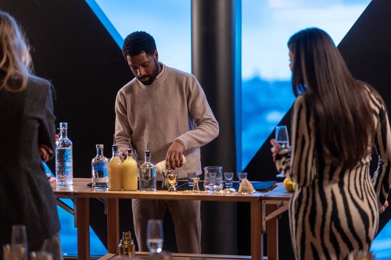 Three people standing at a table with bottles and glasses on it.