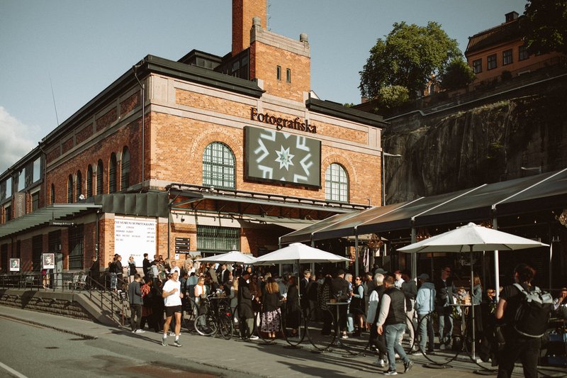 One of the exhibition- halls at the museum for modern photography, Fotografiska in Stockholm. Visitors are looking around in a white, stark gallery space.