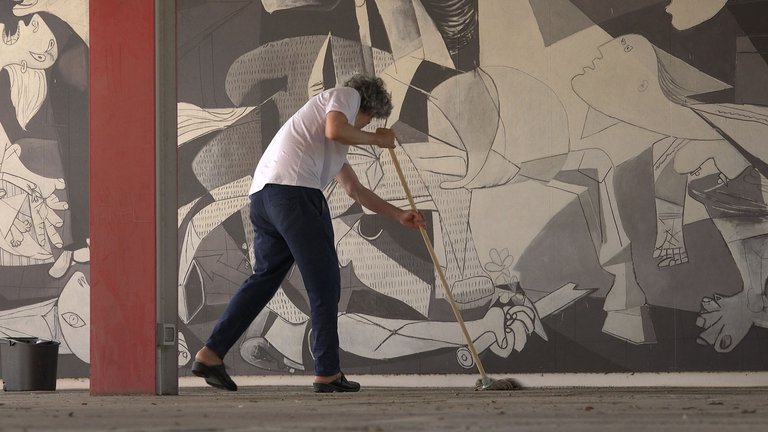 a person cleaning the floor beside the painting Guernica