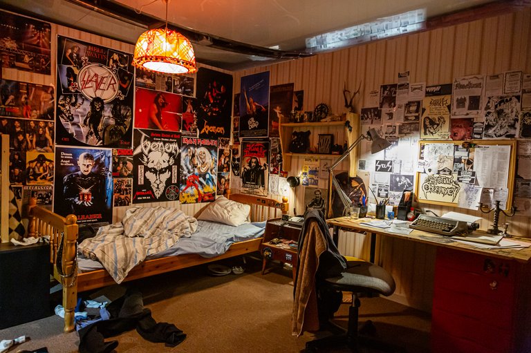 Exhibition decor built as a teenager's room with a messy bed, clothes strewn on the floor, and a number of metal band posters on the walls such as Venom and Slayer.