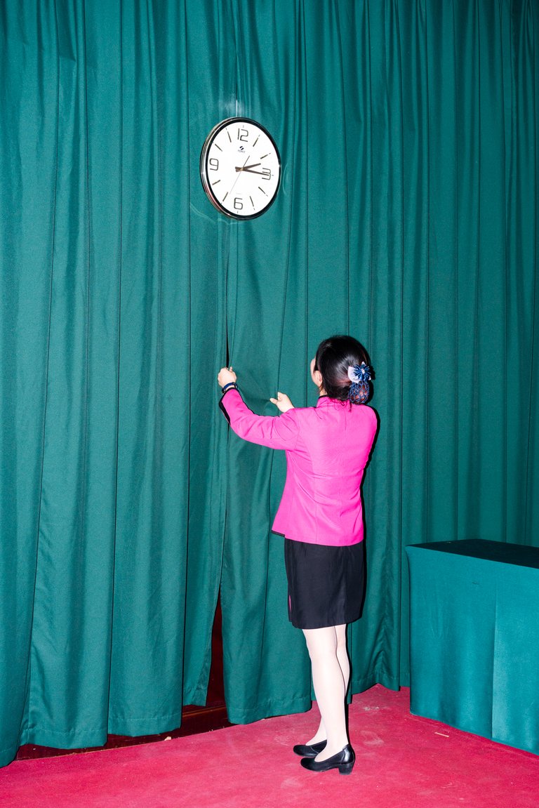 a woman looking at a clock hanging on the curtain