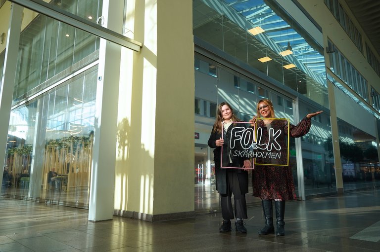 Two people holding a sign "FOLK i Skärholmen"