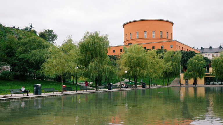 The public library in Stockholm. A cloudy spring day. People are seen in the park adjacent to the iconic building.