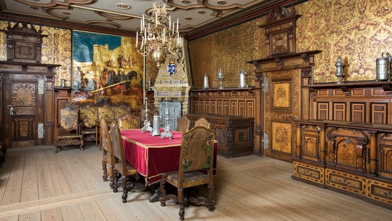 Oxenstiernska salen at Ulriksdals slott, interior. A large room is decorated with massive wooden furniture pieces and gilded wallpaper.