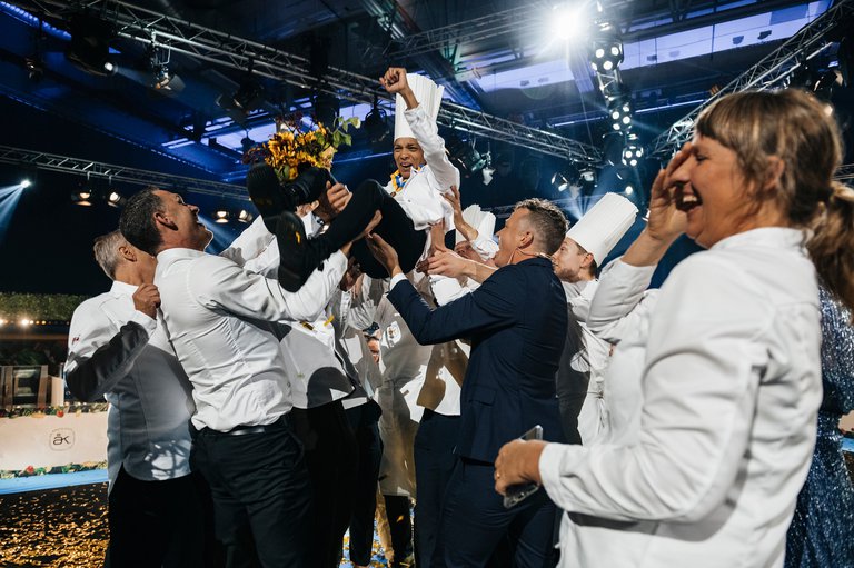 A group of people lifting up in their arms the winner of the competition Chef of the Year.