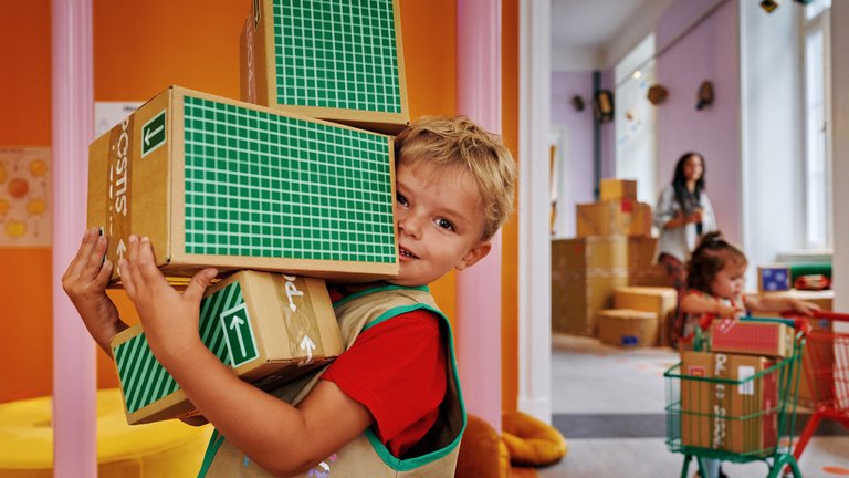 A boy is holding a stcak of cardboard boxes at Postmuseum in Stockholm.