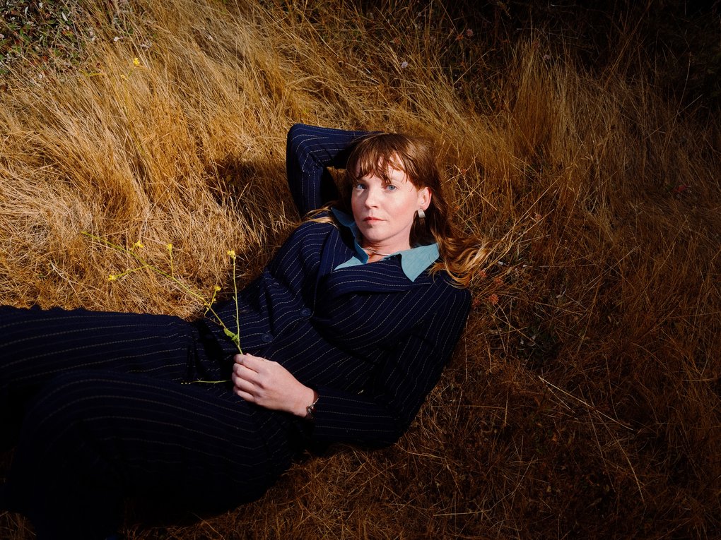 A woman in a dark blue dress, lying on a bed of grass.