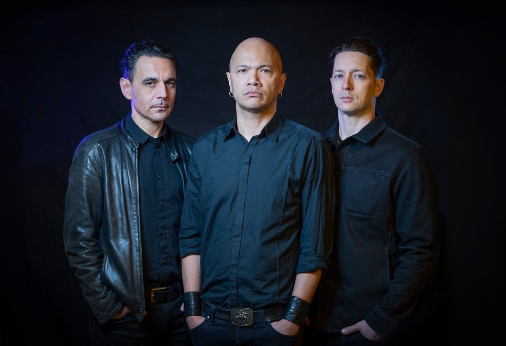 Three men in black shirts against a black backdrop.