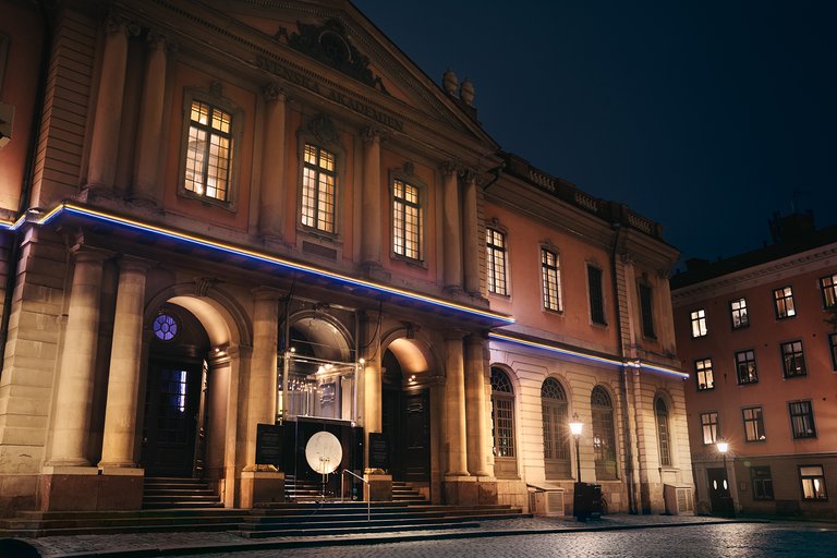 A historical, beige building on a dark winter evening. Several light sources illuminate the facade.