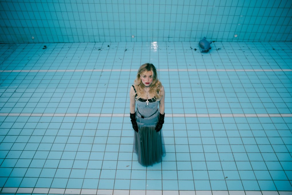 Eileen Alister, in a pink dress, standing at the bottom of an empty swimming pool.