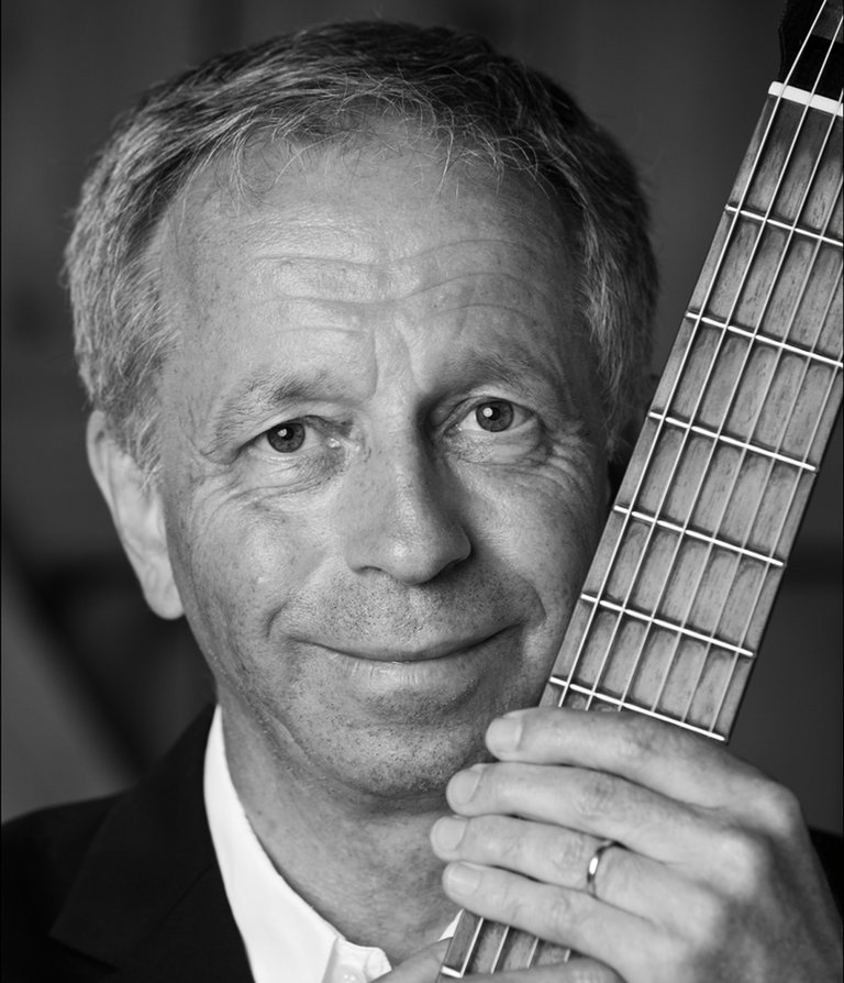 A portrait of the musician Göran Söllscher holding his guitar.