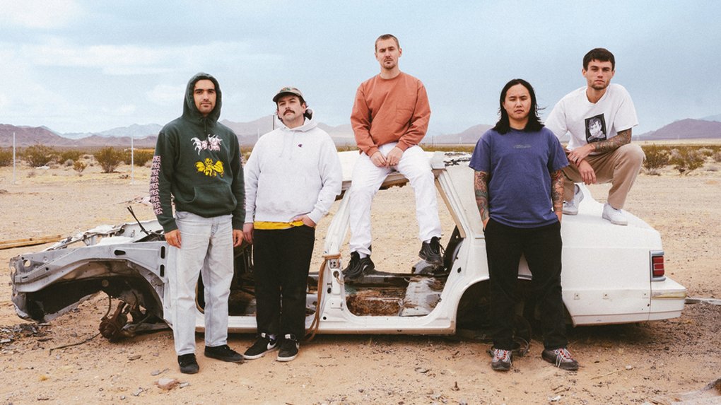 The five members of Militarie gun, posing by the stripped bodywork of a car.