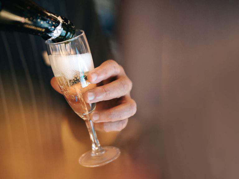 A hand holding a glass that is being filled with champagne.