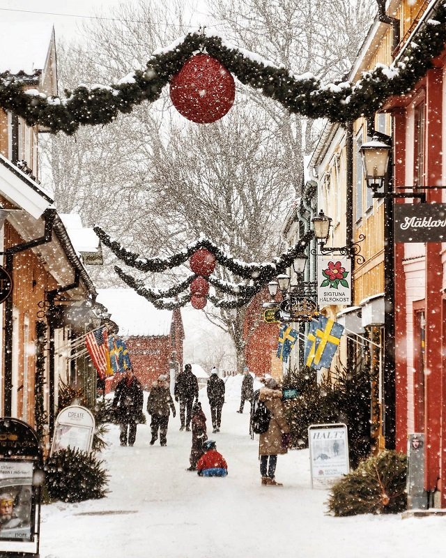 People walking down a snowy small-town street with Christmas decorations.