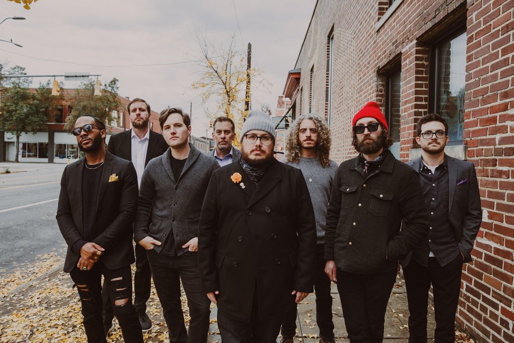 The eight members of Saint Paul & the Broken Bones standing on a sidewalk covered with fallen autumn leaves.