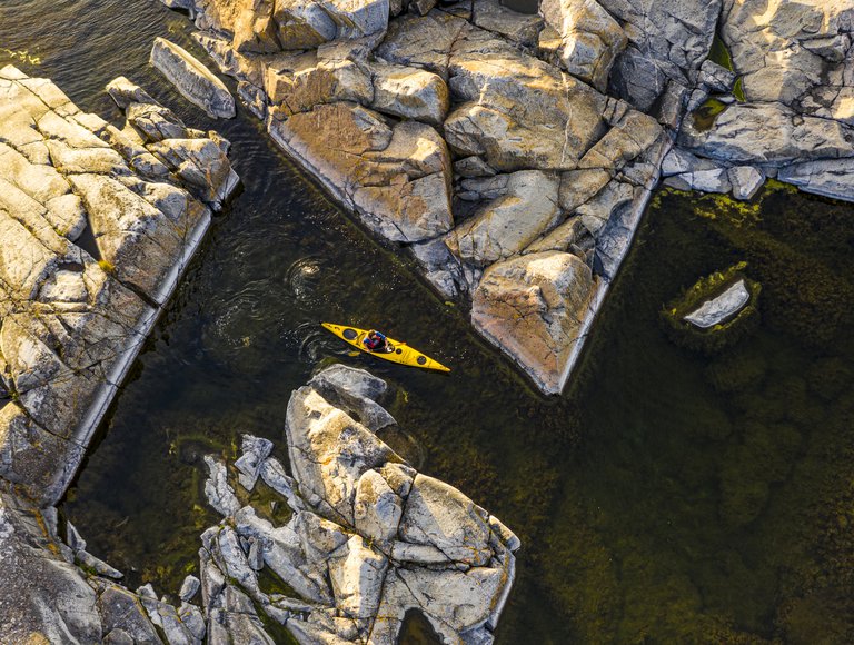 A yellow kayak navigating through rocks at sunset.