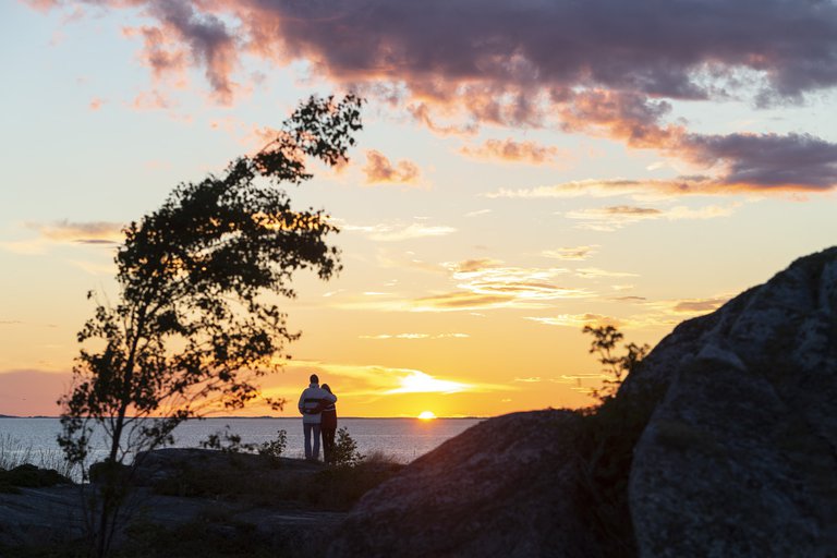 Two people watching the sunset among trees and rocks.