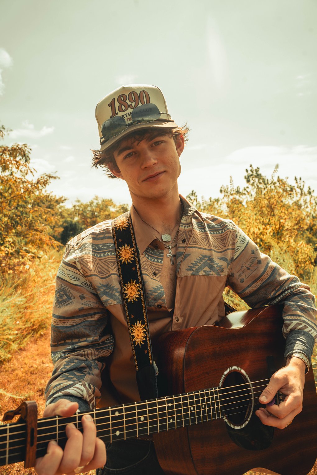 A young man playing guitar outside, in nature.